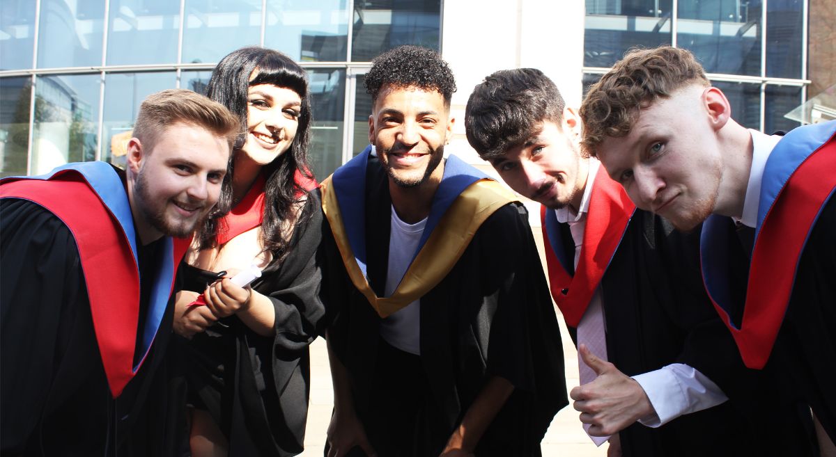 Four SERC Performing Arts Graduates in gowns with Gyasi Sheppy in team talk huddle